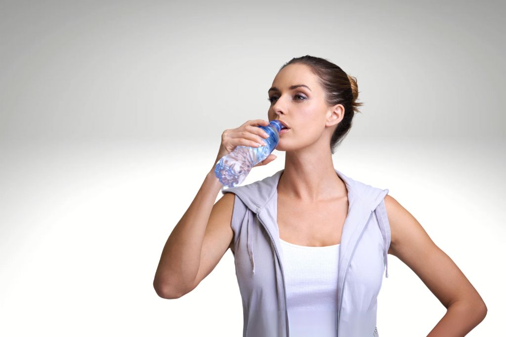 young woman drinking water on a gray background
