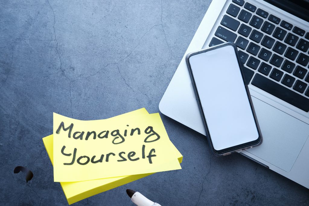 managing yourself text on sticky notes beside the laptop and the mobile phone