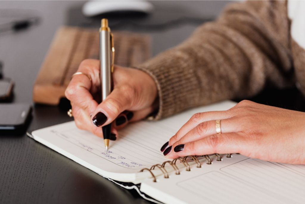 woman in brown long sleeved shirt holding as pen writing down notes